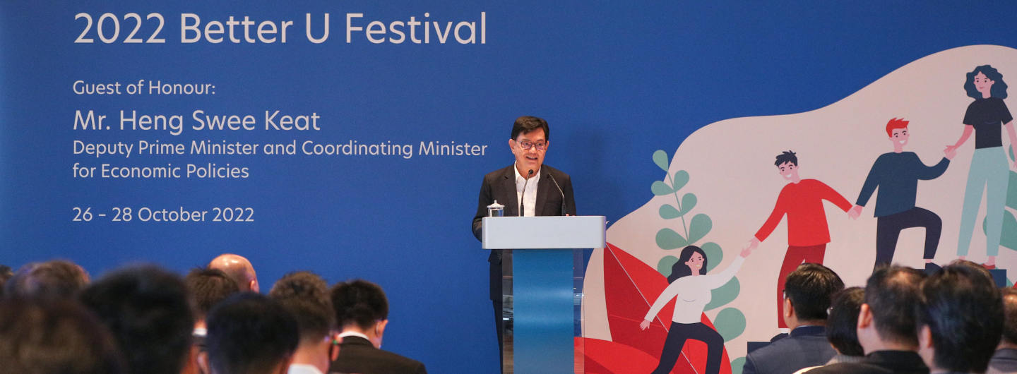 Mr. Heng Swee Keat at the 2022 Better U Festival, with illustrated figures on a blue backdrop. Audience seated.